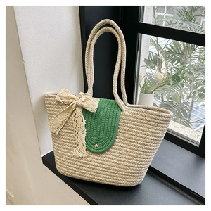 Detail of hand-woven straw tote bag with green flap and beige lace bow decoration