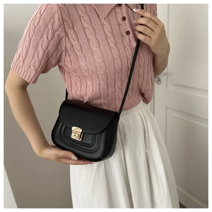 Detail of a black crossbody saddle bag with gold metal lock on a female model