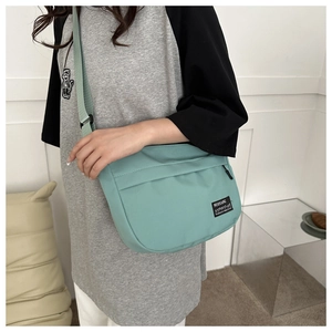 Detail of mint green nylon crossbody bag showing the woven logo and adjustable shoulder strap