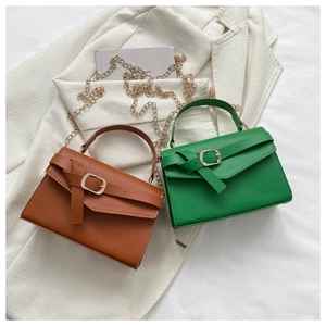 Flat lay of brown and green leather handbags with gold chain straps on white fabric