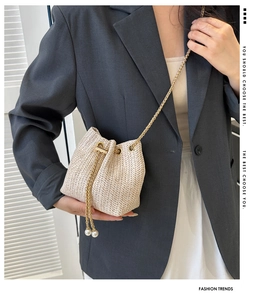 Détail d'un sac seau en paille tressée avec chaîne dorée et perles blanches