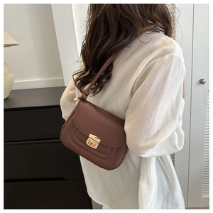 Close-up of brown leather crossbody bag with gold metal push lock on a female model