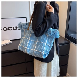 Close-up of blue and white checkered knit tote bag with tassel trim and leather handle
