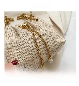 Détail du sac seau tissé beige avec cordon en chaîne dorée et perles élégantes