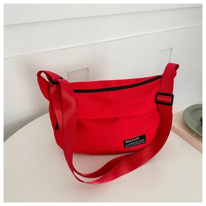 Detail of red oxford fabric crossbody bag with wide shoulder strap and brand label