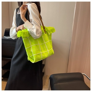 Neon green knit tote bag with fringe details and leather handles shown on a model