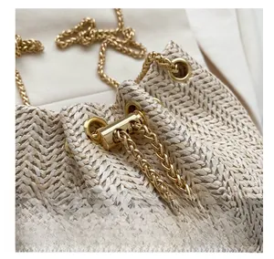 Détail d'un sac seau tressé beige avec bandoulière chaîne dorée et cordon de serrage métal
