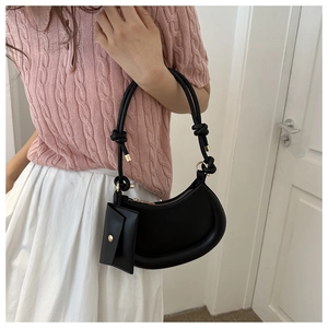 Detail of matte black crescent underarm bag with thick knotted strap and mini pouch charm