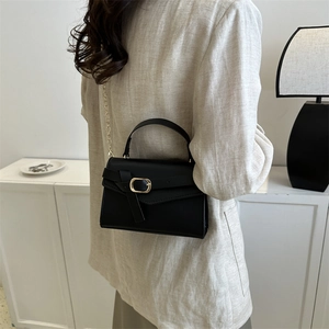 Minimalist black square handbag with top handle and gold chain strap worn by a model