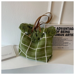 Detail of green woven tote bag featuring white grid patterns and fringed top edges