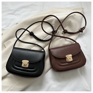 Close-up of minimalist crossbody bags in black and coffee with gold locks on beige blazer