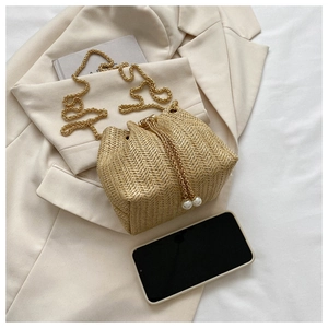 Détail du sac seau tressé avec chaîne dorée et élégantes perles blanches sur le cordon