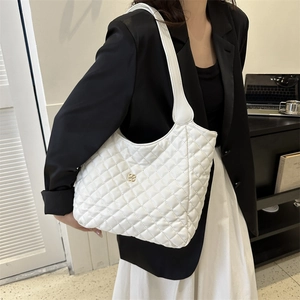 White quilted crossbody tote bag with gold floral logo worn by model in black suit