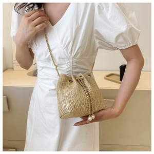 Détail du sac seau tressé beige avec cordon perlé et bandoulière chaîne dorée