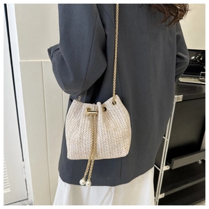 Detail of woven straw bucket bag with gold chain and white pearl drawstring tassels