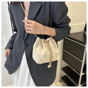 Détail du sac seau tressé crème avec bandoulière dorée et accents de perles au cordon