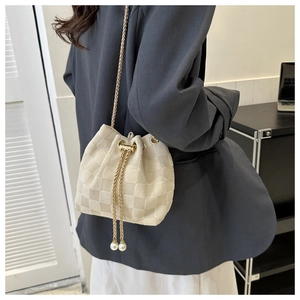 Détail du sac seau tressé beige avec bandoulière chaîne dorée et breloques en perles