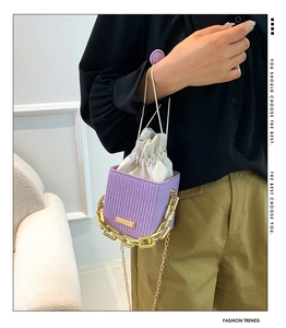 Close-up of purple woven bucket bag with white drawstring lining and gold chain strap