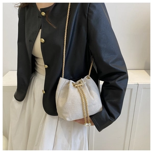 Détail d'un sac seau tressé avec cordon de perles et bandoulière chaîne dorée