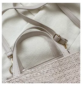 Detailed close-up of beige straw woven bag with faux leather strap and golden metal buckle