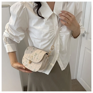 Detail of saddle bag featuring beige woven texture and green floral embroidery with gold lock