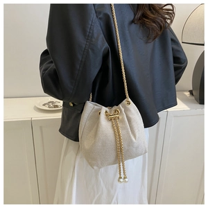 Detail of woven bucket bag featuring gold chain strap and pearl drawstring accents