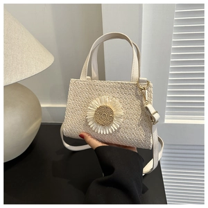 Detail of cream woven straw crossbody bag featuring a 3D floral accent and strap