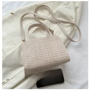 Detailed comparison of the woven straw shoulder bag size next to a mobile phone