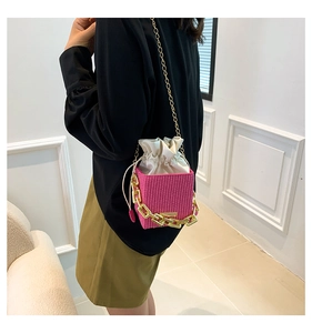 Pink woven square crossbody bag with drawstring closure and golden chain detail on model