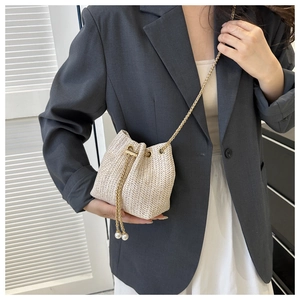 Détail du sac seau en paille beige avec texture tissée fine et détails de perles au cordon