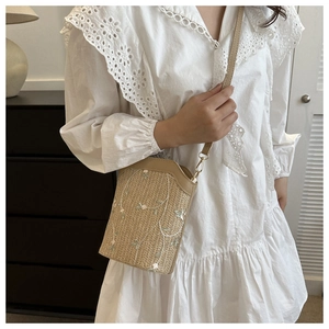 Detail of woven straw bag with floral embroidery and brown leather trim on lace dress
