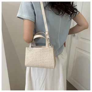 Model wearing a woven straw shoulder bag with leather straps and cream white texture