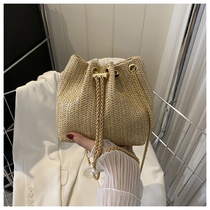Détail du sac seau en paille tressée avec chaîne dorée et décoration en perle