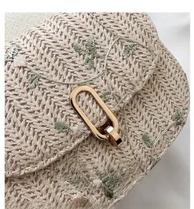 Detailed macro view of woven straw saddle bag featuring green leaf embroidery and gold buckle
