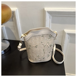 Detail of straw woven bucket bag with floral embroidery and white leather strap