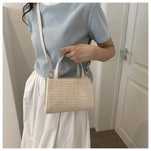 Close-up of cream woven straw bag texture with detachable strap worn by model