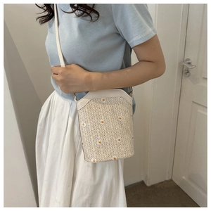 Detailed view of daisy embroidery on woven straw bucket bag with slim leather strap