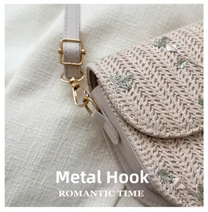 Detail of golden metal hook and straw weaving on beige crossbody saddle bag
