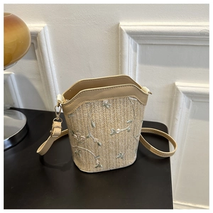 Detailed close-up of intricate white floral embroidery on a woven straw bucket bag