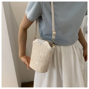 Detail of cream straw bucket bag featuring yellow daisy floral embroidery and white leather strap