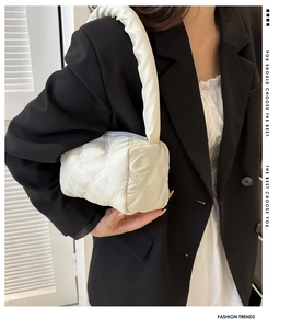 Detail of white quilted cylindrical bag featuring textured pleated handle and zipper