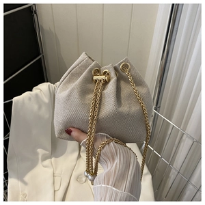Détail du sac seau tissé avec élégante bandoulière dorée et accent de perle fine
