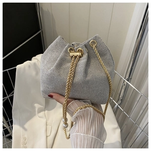 Détail d'un sac seau tissé avec bandoulière en chaîne dorée et décor de perles