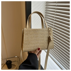 Detail of handwoven beige straw square bag with faux leather handle and gold hardware