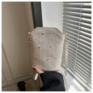 Detail of straw woven crossbody bag featuring delicate daisy embroidery and white strap
