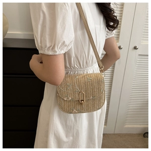 Close-up of woven straw crossbody bag with floral embroidery and gold turn-lock