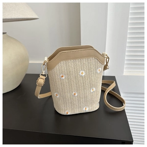 Detail of straw woven bag featuring daisy floral embroidery and leather strap