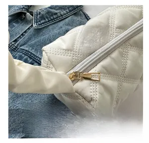 Macro view of a smooth gold metal zipper on a white quilted nylon shoulder bag