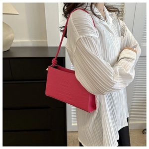 Détail d'un sac porté épaule rouge rose avec motif crocodile et nœud sur la sangle