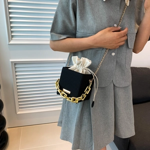 Black striped crossbody bag with gold chain and white drawstring pouch in indoor setting